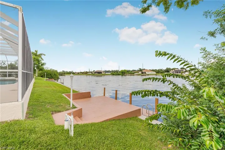 View of dock with glass enclosure, a water view, and a lawn