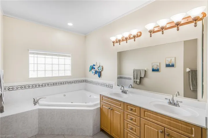 Primary Bathroom featuring vanity, a relaxing tiled tub, and ornamental molding