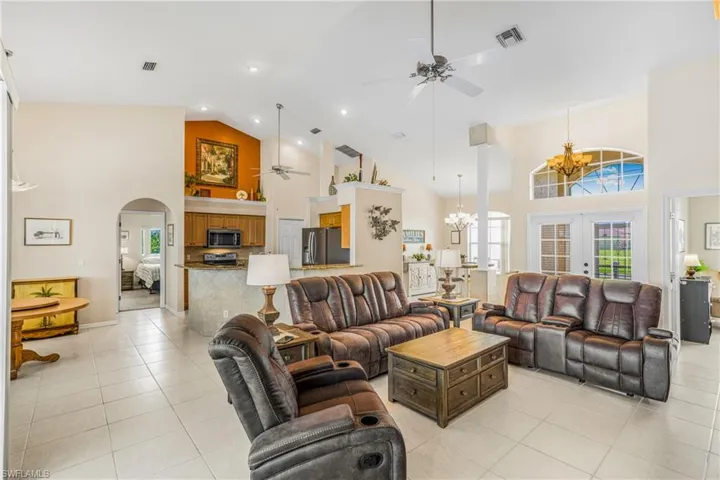Tiled living room featuring french doors, ceiling fan with notable chandelier, and high vaulted ceiling