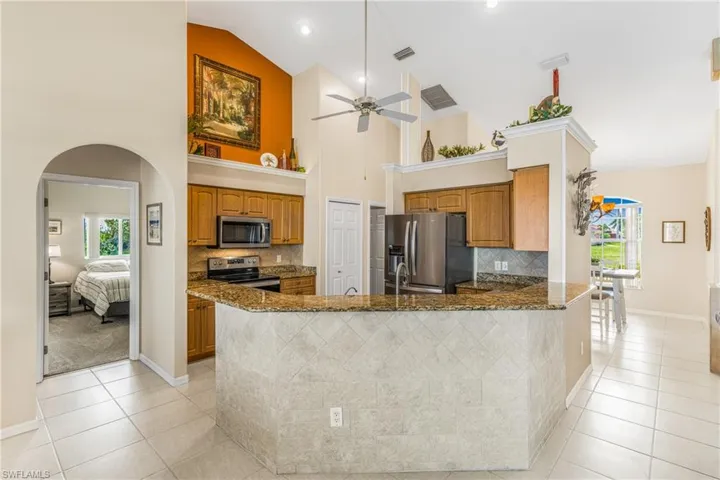 Kitchen featuring kitchen peninsula, high vaulted ceiling, stainless steel appliances, light tile patterned floors, and dark stone countertops