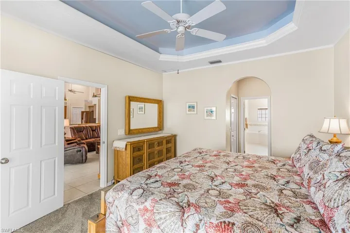 Carpeted bedroom with ornamental molding, ceiling fan, a raised ceiling, and ensuite bathroom