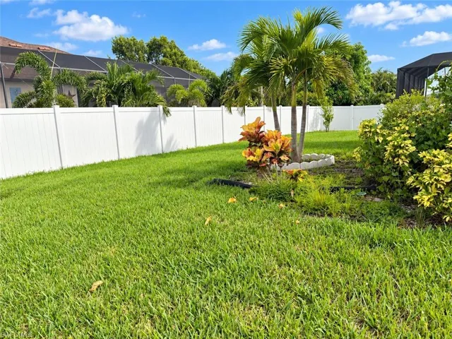 Expansive green lawn, white privacy fencing, and tropical landscaping with palm trees