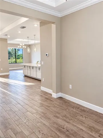 Wood-finish tile flooring throughout, crown molding, tray ceiling, recessed lighting, and a kitchen island with pendant lighting