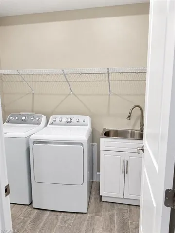Laundry area featuring wood-finish flooring, white cabinetry with silver hardware, a stainless steel sink, and wire shelving