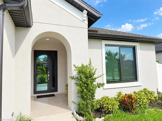 Arched entryway with a modern front door, stucco exterior, and a dark shingle roof