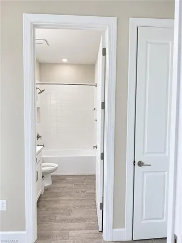 Bathroom featuring a tiled tub/shower combination with recessed niche, white vanity, and wood-finish flooring