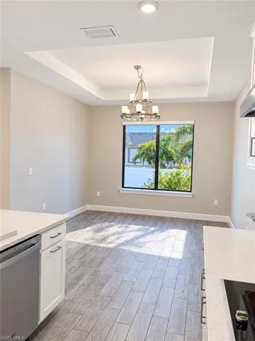 Tray ceiling with recessed lighting and a chandelier, wood-finish flooring, and a large window