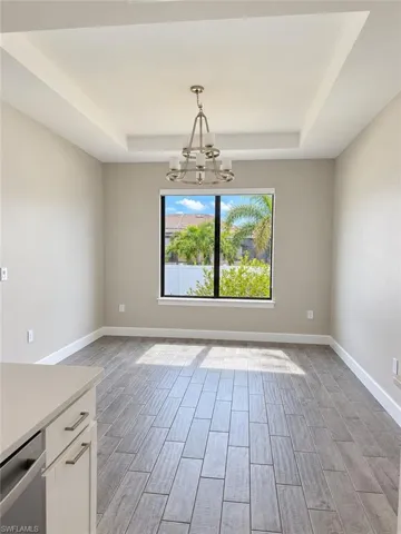 Tray ceiling with a brushed nickel chandelier, large window, and wood-finish tile flooring