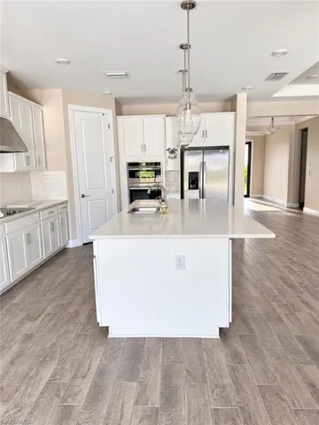 Kitchen featuring an island with a light-toned countertop, stainless steel appliances, white cabinetry, and wood-finish flooring