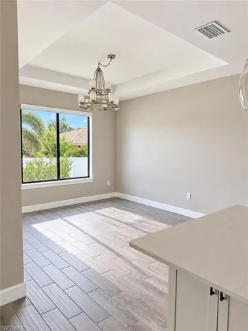 Tray ceiling with a chandelier, large window with a white frame, light wood-finish flooring, and light-colored walls