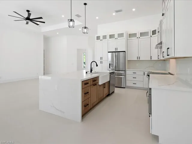 Kitchen with glass insert cabinets, light stone countertops, appliances with stainless steel finishes, hanging light fixtures, and white cabinets