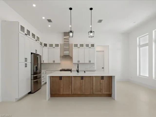 Kitchen with glass insert cabinets, stainless steel refrigerator with ice dispenser, light stone counters, a center island with sink, and recessed lighting