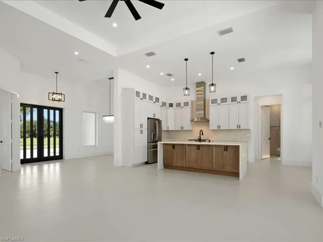 Kitchen with open floor plan, a spacious island, wall chimney range hood, stainless steel refrigerator with ice dispenser, and a high ceiling