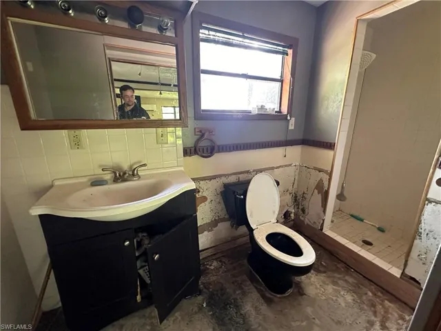 Bathroom featuring walk in shower, vanity, tile walls, and toilet