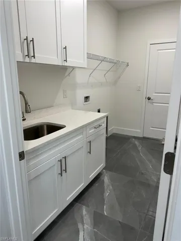 Laundry area featuring cabinets, sink, dark tile flooring, and washer hookup