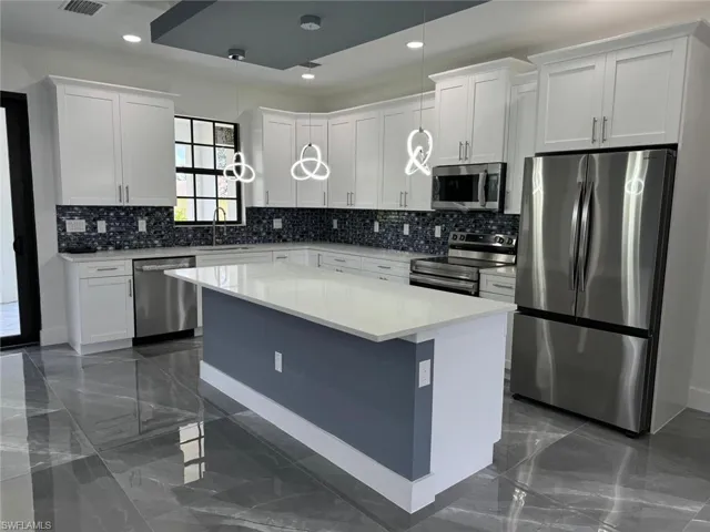Kitchen featuring tasteful backsplash, a kitchen island, hanging light fixtures, white cabinets, and appliances with stainless steel finishes
