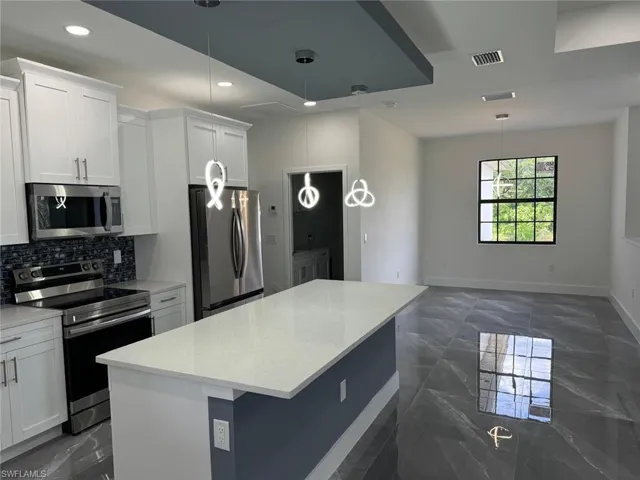 Kitchen featuring a center island, white cabinetry, stainless steel appliances, light stone counters, and dark tile flooring