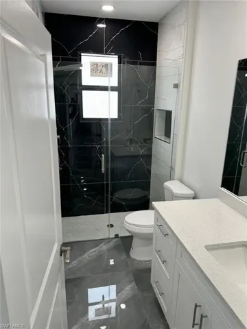 Bathroom with tile flooring, a shower with shower door, toilet, and vanity