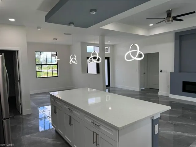 Kitchen with decorative light fixtures, a fireplace, a kitchen island, ceiling fan with notable chandelier, and light stone countertops