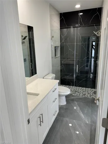 Bathroom featuring a shower with door, tile flooring, vanity, and toilet