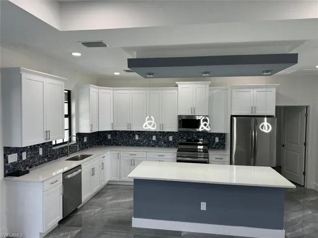 Kitchen featuring tasteful backsplash, stainless steel appliances, a kitchen island, sink, and white cabinetry