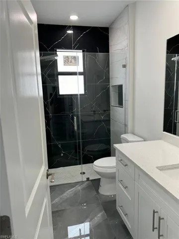 Bathroom featuring tile flooring, walk in shower, vanity, and toilet