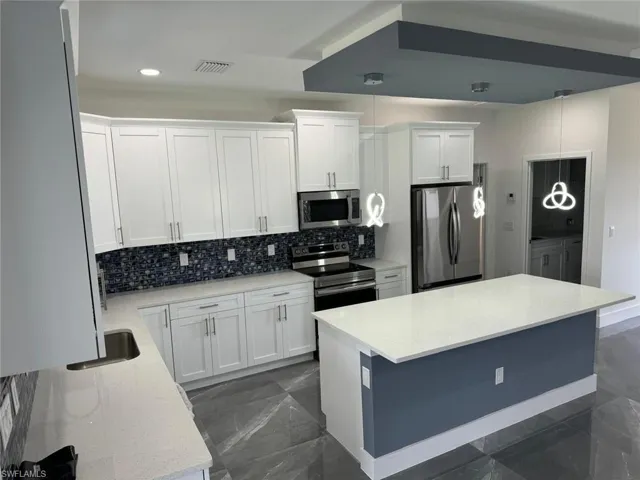 Kitchen with stainless steel appliances, white cabinets, tasteful backsplash, and pendant lighting