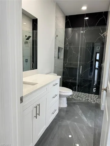 Bathroom featuring tile floors, a shower with door, vanity, and toilet