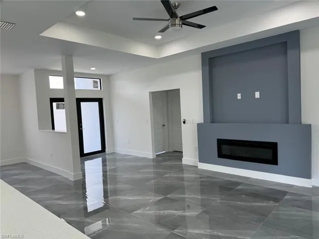 Living room featuring a tray ceiling, dark tile floors, ceiling fan, and a fireplace