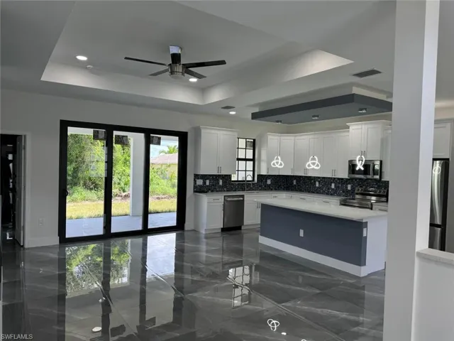Kitchen with a raised ceiling, ceiling fan, stainless steel appliances, and white cabinets