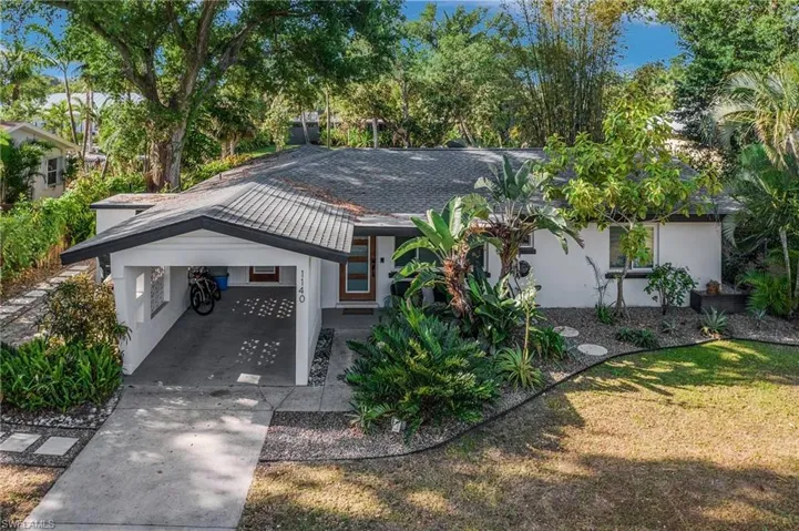 View of front facade featuring an attached carport, driveway, stucco siding, and a shingled roof