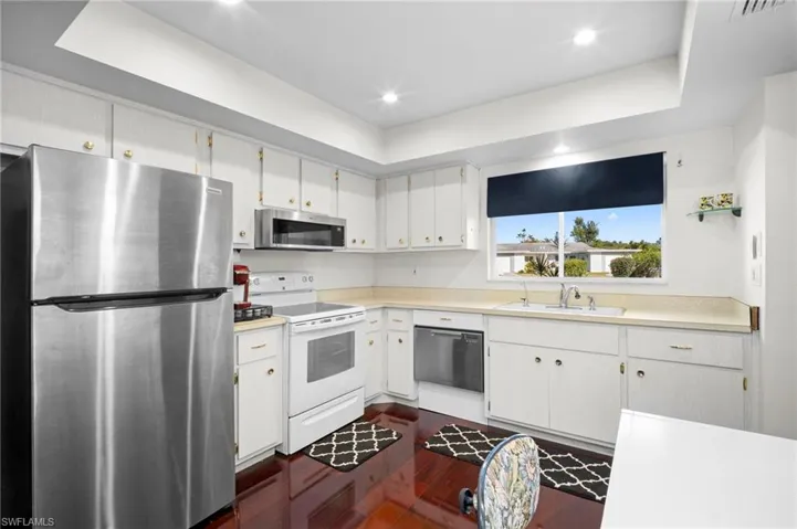 Kitchen with stainless steel appliances, a tray ceiling, light countertops, dark wood-style flooring, and white cabinetry