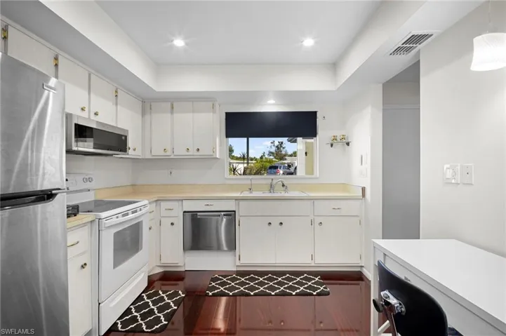 Kitchen featuring stainless steel appliances, light countertops, white cabinetry, a raised ceiling, and decorative light fixtures
