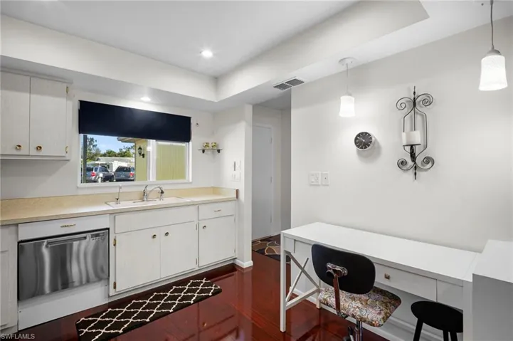 Kitchen featuring light countertops, white cabinets, stainless steel dishwasher, and hanging light fixtures