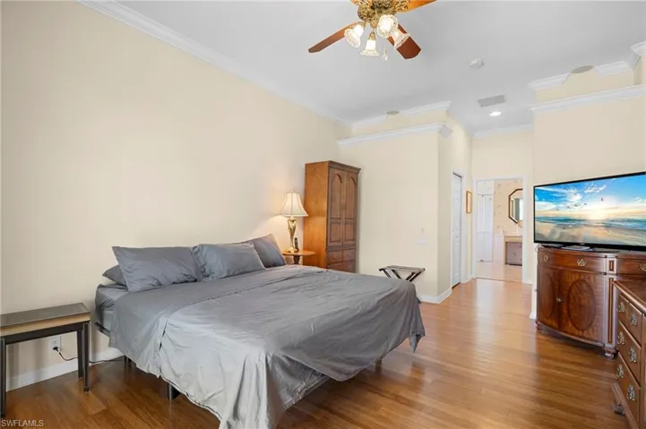 Bedroom with crown molding, light wood-style flooring, ensuite bath, a ceiling fan, and a closet