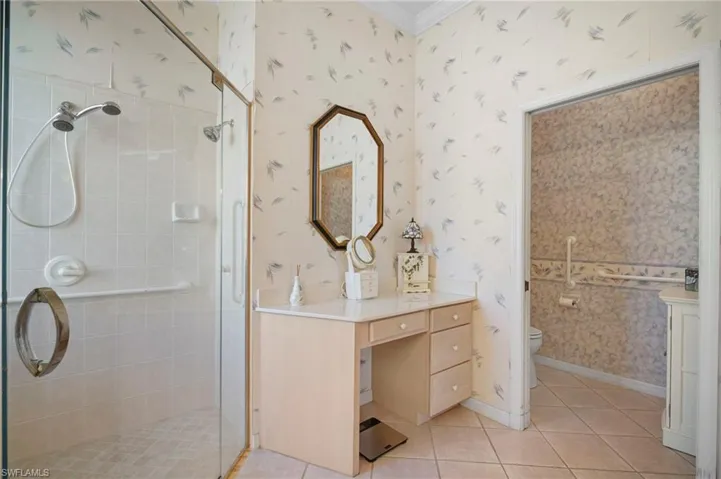 Bathroom with wallpapered walls, a shower stall, vanity, light tile patterned floors, and crown molding