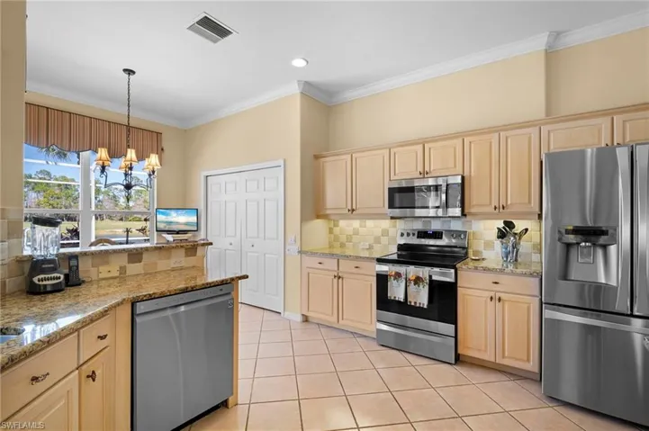 Kitchen featuring stainless steel appliances, light stone countertops, a chandelier, light wood finish cabinetry, and crown molding