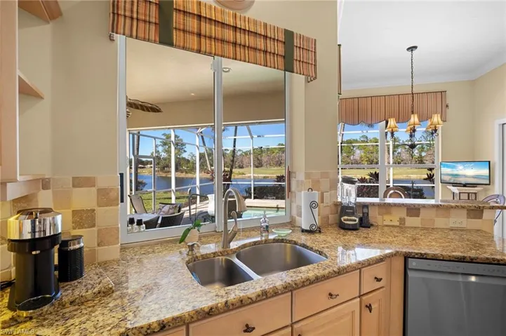 Kitchen featuring dishwasher, light stone countertops, hanging lights, light wood finish cabinetry, and a sunroom
