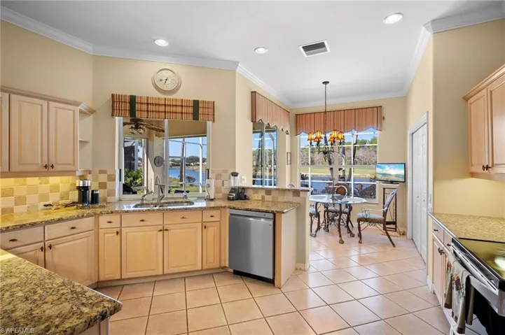 Kitchen with light wood finish cabinetry, a chandelier, stainless steel appliances, light stone counters, and healthy amount of natural light
