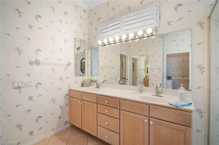 Bathroom with double vanity, wallpapered walls, light tile patterned floors, and crown molding