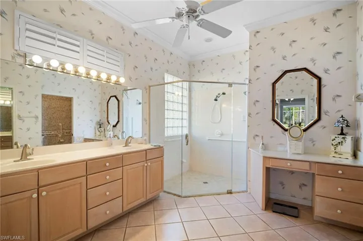 Full bathroom featuring a shower stall, double vanity, wallpapered walls, ornamental molding, and a ceiling fan