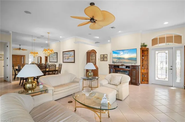 Living room featuring a ceiling fan, light tile patterned flooring, ornamental molding, and a chandelier