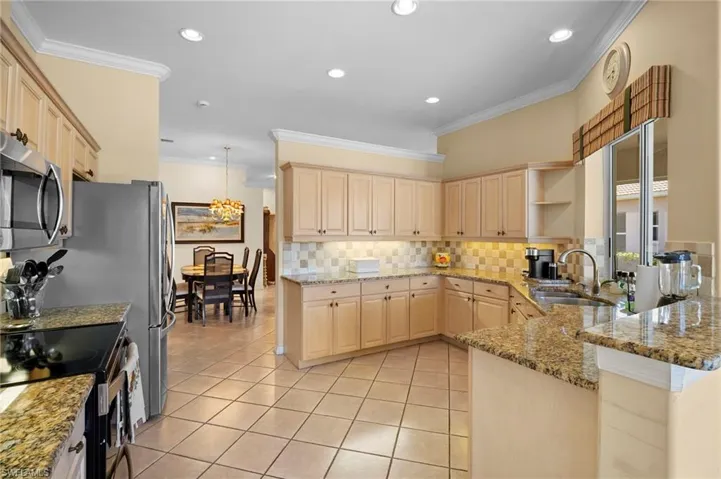 Kitchen with light stone counters, crown molding, stainless steel appliances, decorative backsplash, and light tile patterned flooring