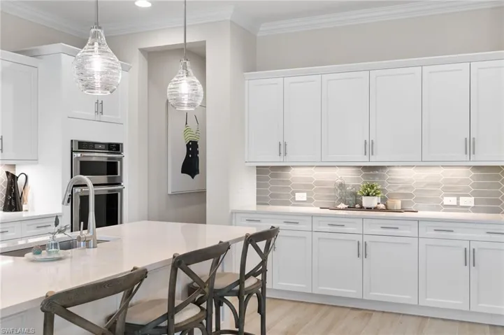 Kitchen featuring white cabinetry, backsplash, crown molding, light wood-style floors, and double oven