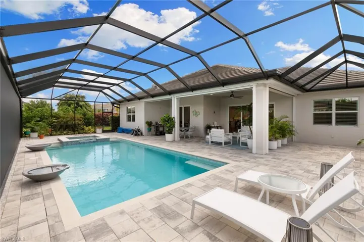 Back of house with a sunroom, a lanai, a pool with connected hot tub, ceiling fan, and stucco siding