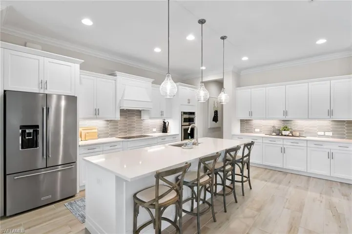 Kitchen with appliances with stainless steel finishes, crown molding, a breakfast bar, white cabinets, and decorative light fixtures