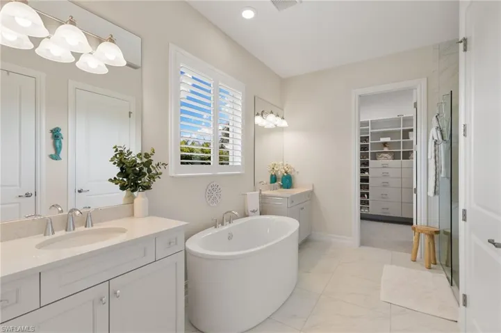 Bathroom featuring two vanities, a freestanding bath, a stall shower, recessed lighting, and light marble finish flooring