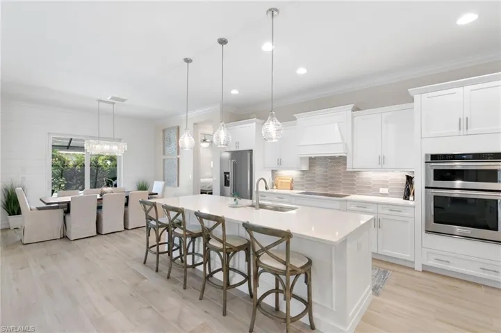 Kitchen with a breakfast bar, tasteful backsplash, decorative light fixtures, white cabinetry, and crown molding