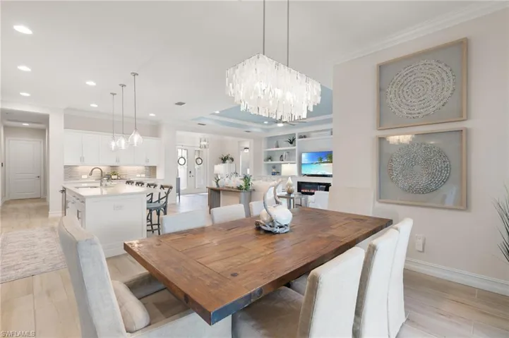 Dining space with light wood-style floors, ornamental molding, a chandelier, a tray ceiling, and recessed lighting