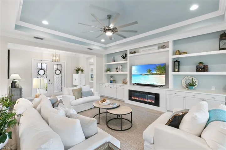 Living area with a tray ceiling, crown molding, recessed lighting, a glass covered fireplace, and light wood-style floors